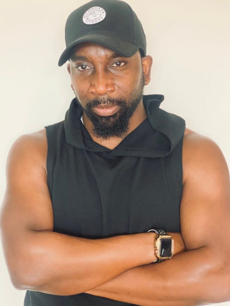 Person wearing a black sleeveless hoodie and cap, arms crossed, photographed against a light background with a composed expression